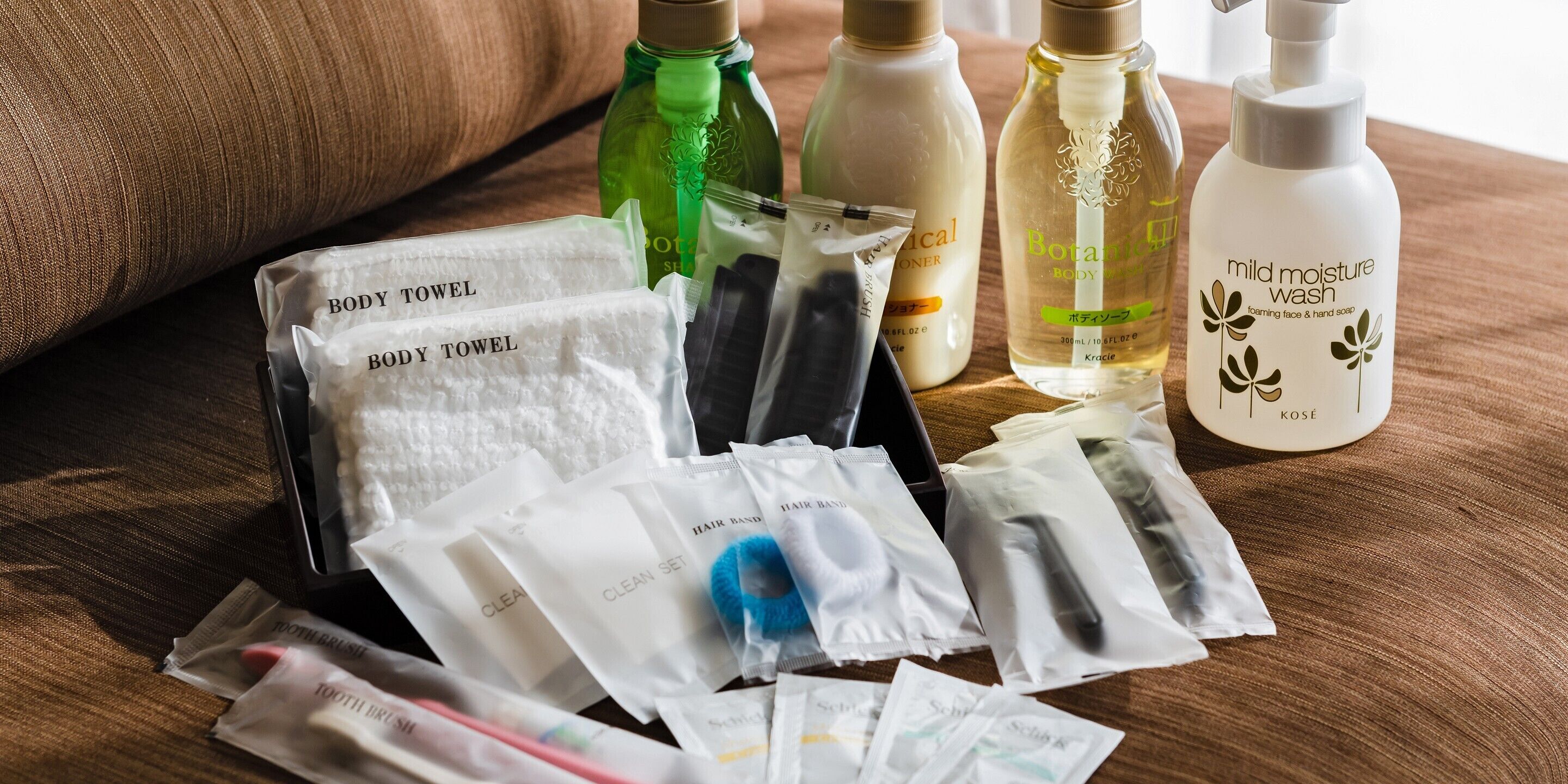 A variety of toiletries and personal care items, including body towels, hair brushes, and bottles of shampoo and body wash, arranged on a wooden surface.