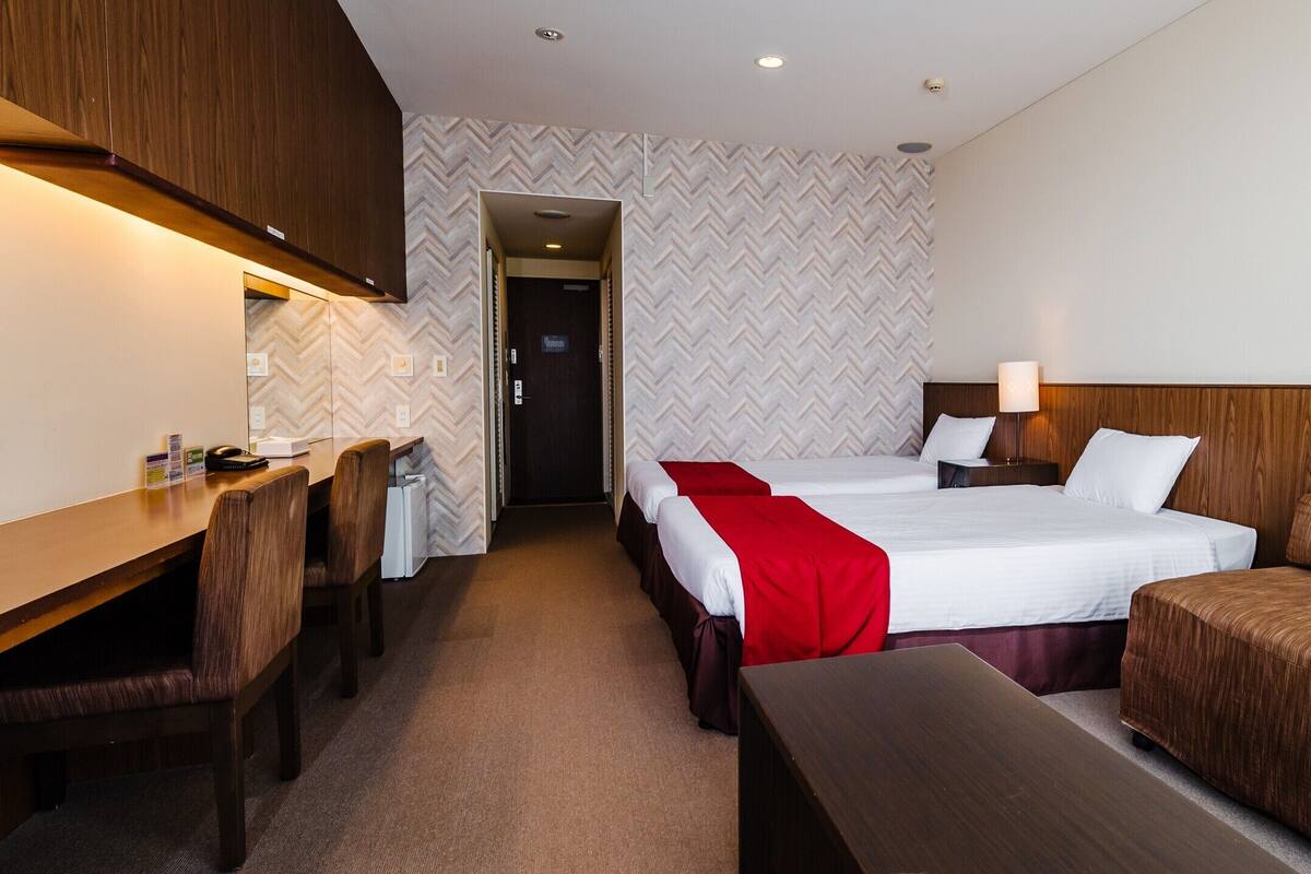 A hotel room with two beds, a desk, and a chair.