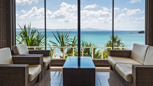 Un balcón con muebles de mimbre y una mesa de vidrio, con vista a una playa y al mar.