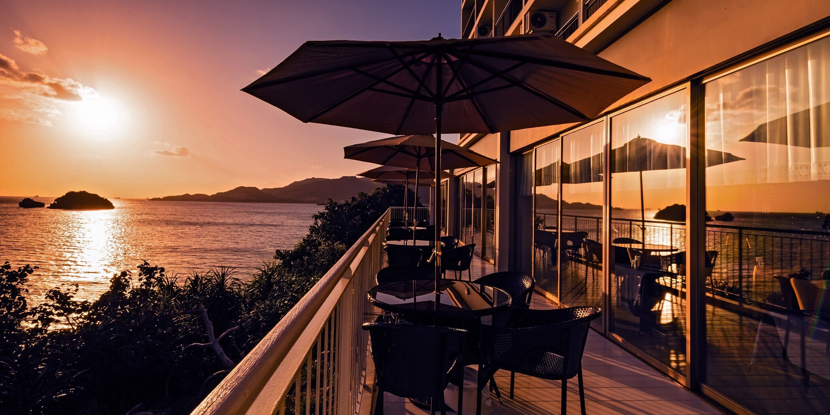 Un balcón con mobiliario exterior y vistas al atardecer sobre el agua.