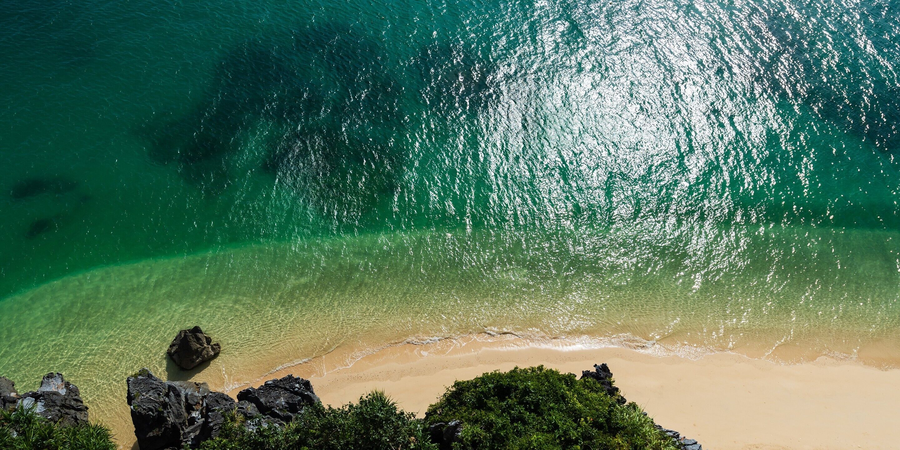 Ein Strand mit klarem türkisblauem Wasser, Sandstrand und Felsformationen.