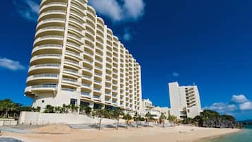 A multi-story hotel with balconies, located near a beach with clear skies.