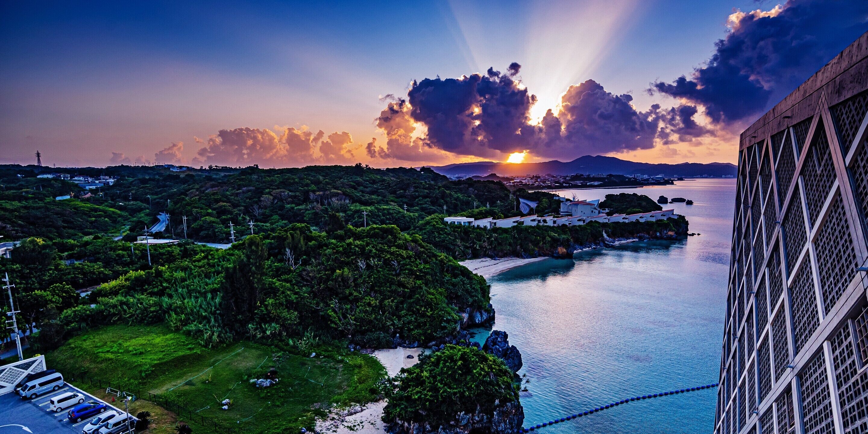 A coastal landscape with a sunset, a bridge, and a building with a grid-like facade.