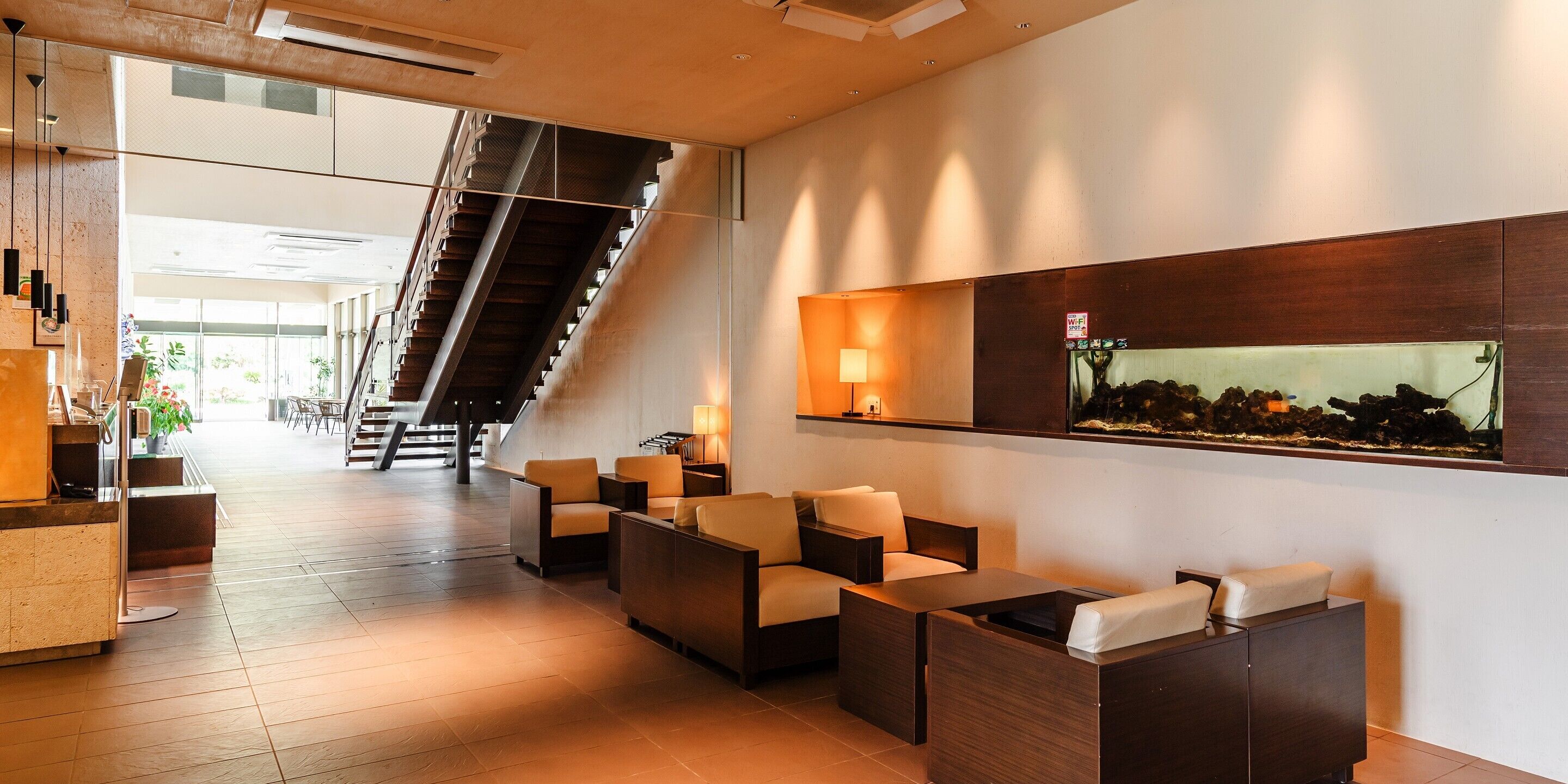 Um lobby moderno com balcão de atendimento, área de estar, escadaria e um grande aquário.