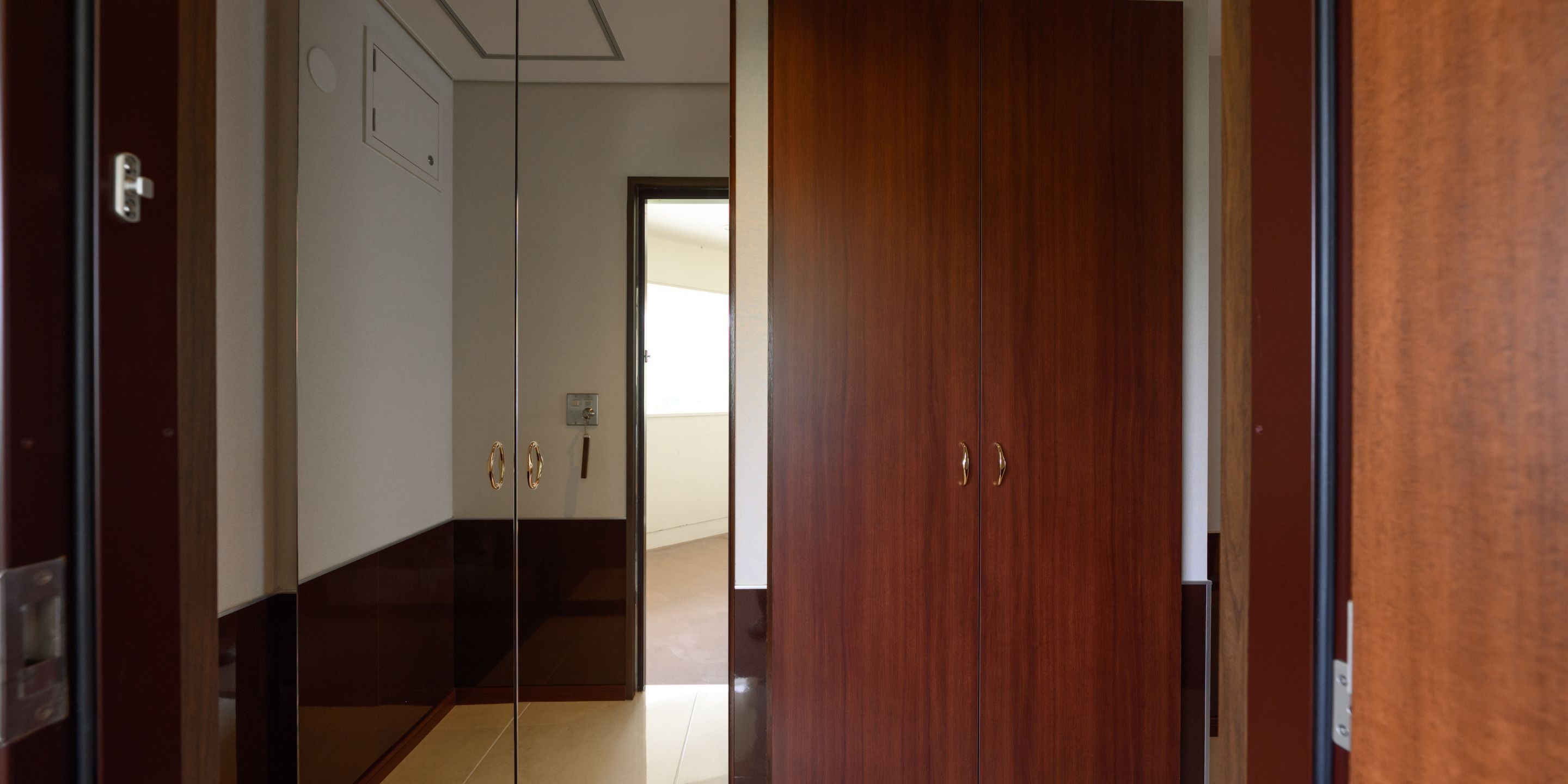 A hallway with a wooden door, a mirror, and a light switch on the wall.