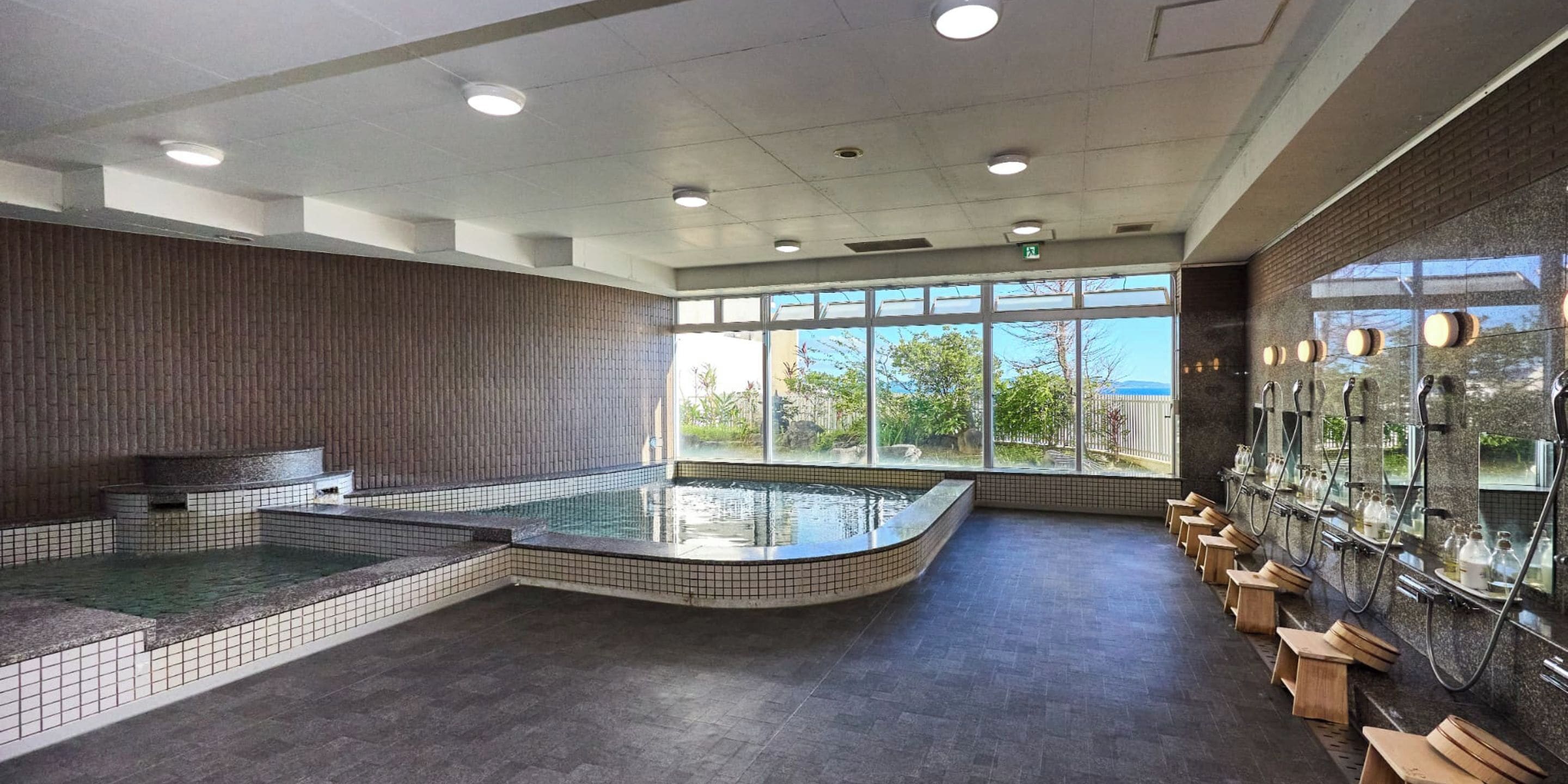 A spa area with a large window, a hot tub, and a row of wooden stools.