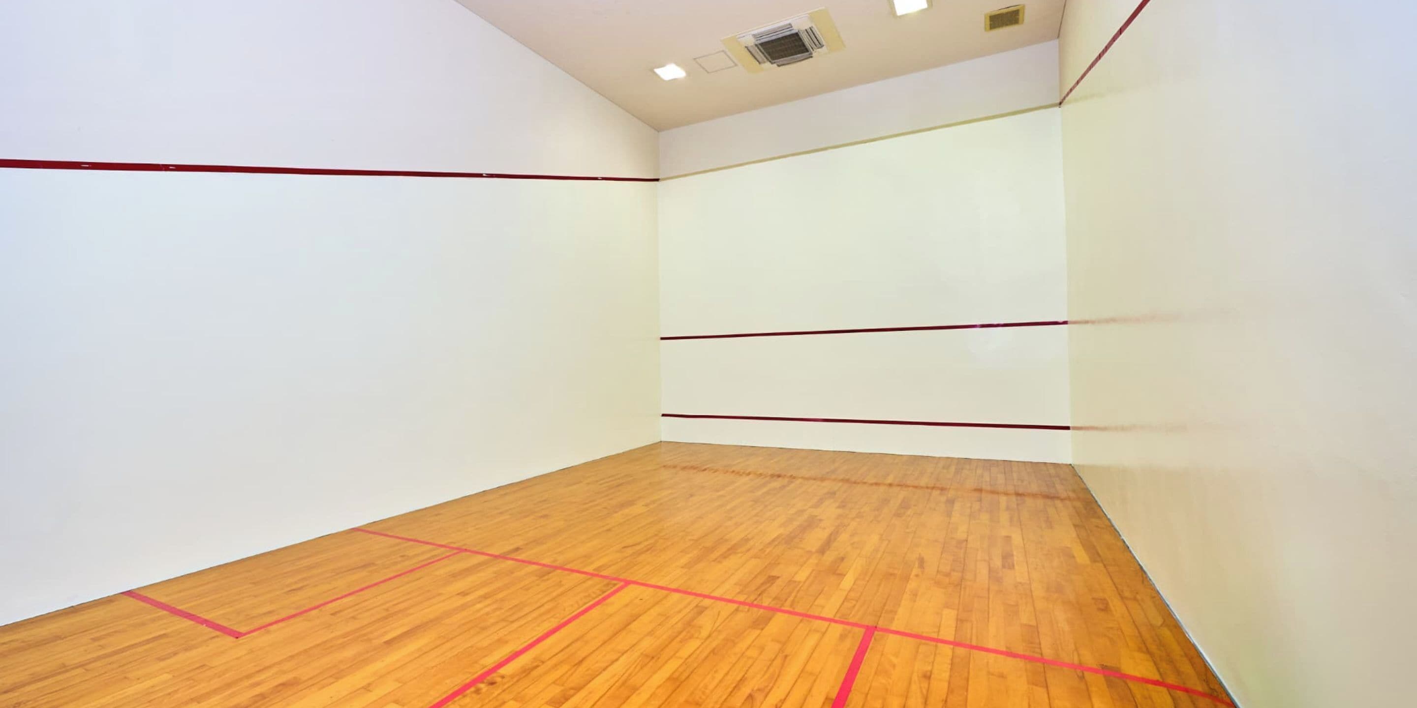 Un court de squash doté d’un plancher en bois et de lignes de démarcation rouges.