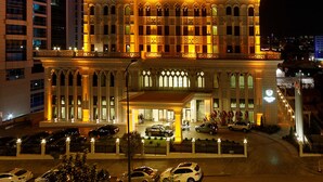 A high-rise hotel with a prominent entrance, multiple balconies, and a parking area with cars. - Meyra Palace (Ankara)