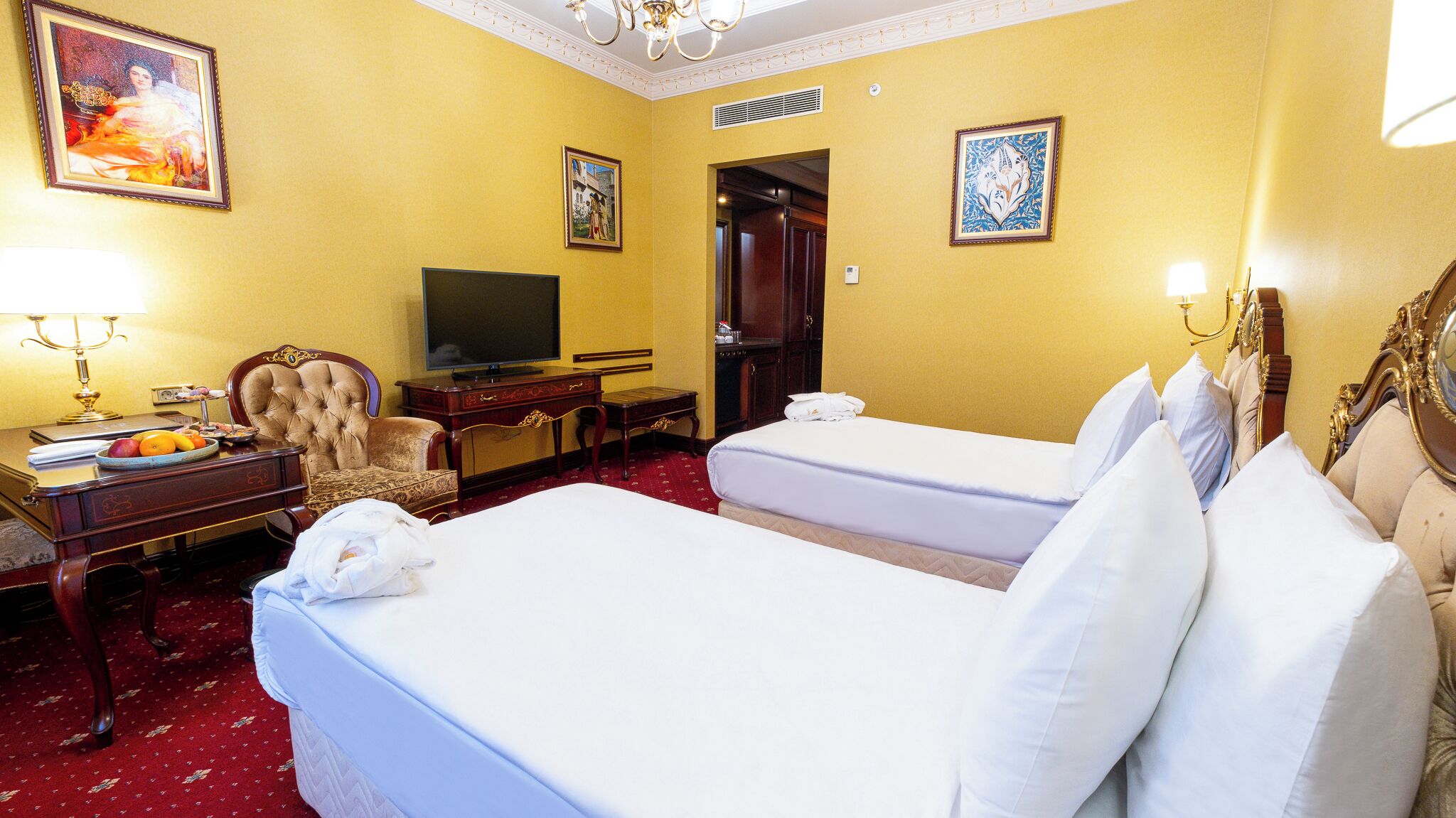Habitación de hotel con dos camas, un escritorio con televisor, una silla y obras de arte en las paredes.