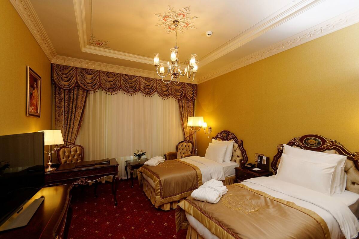 A hotel room with two beds, a desk, a television, and a chandelier.
