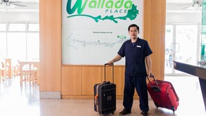 Una persona con uniforme azul sostiene dos maletas, de pie frente a un cartel que dice 'Wallada Place' y un mapa.