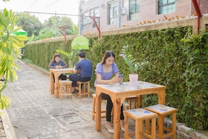 A courtyard with wooden tables and chairs, a hedge, and a building in the background. - Wallada Place (Bangkok)