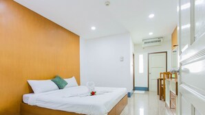 Habitación de hotel con cabecera de madera, cama bien hecha con sábanas blancas, una mesita con silla y un espejo en la pared.