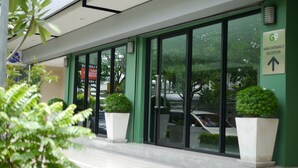 A modern building with large glass doors, a green wall, and a sign indicating the main entrance. - G9 Bangkok (Bangkok)