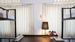 A hotel room with two bunk beds, a table with a tray of cups, a lamp, and a vase with flowers. - G9 Bangkok (Bangkok)