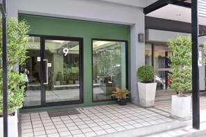 A modern building entrance with a green door, large windows, and potted plants.