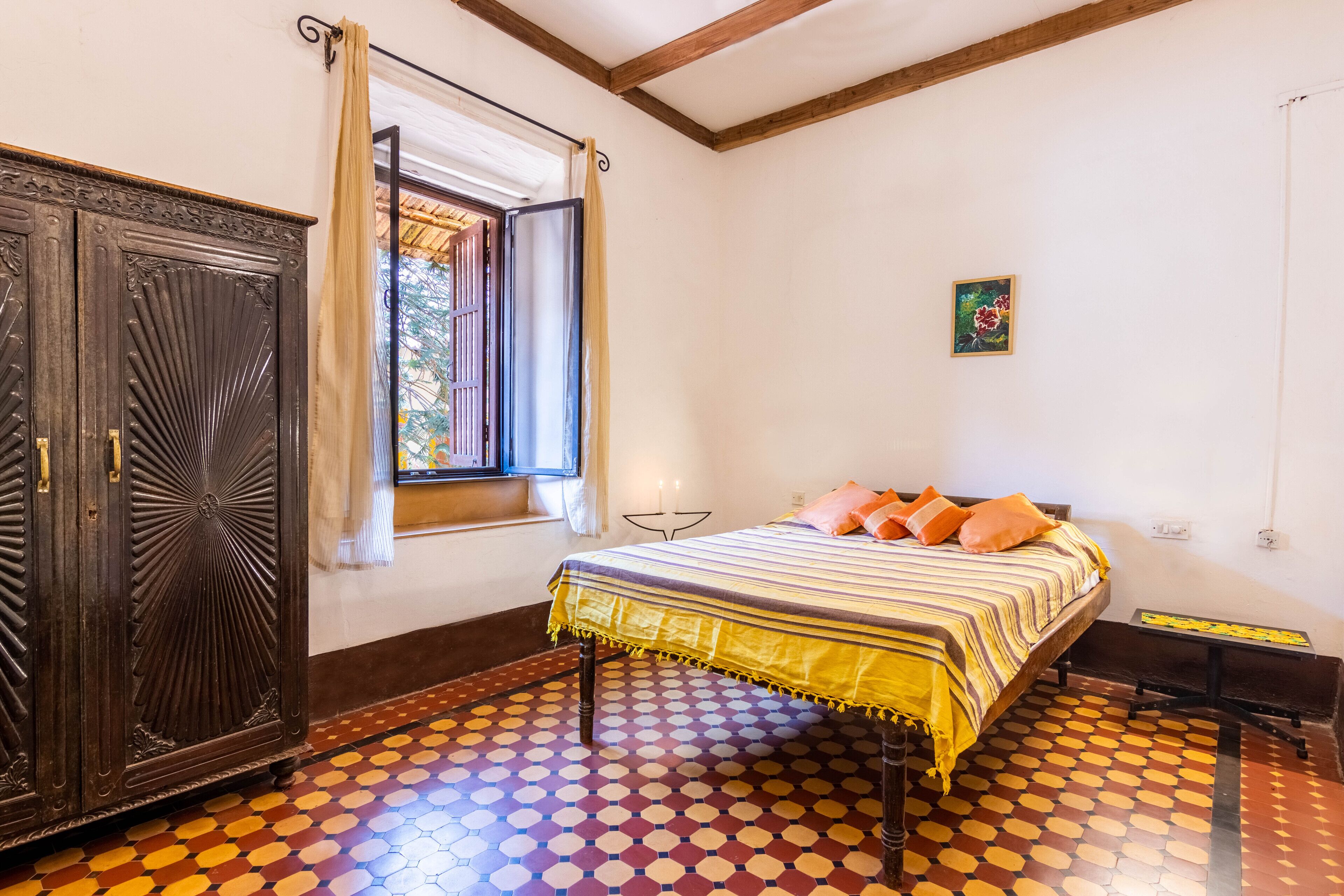 A bedroom with a bed, a wardrobe, a window with curtains, a painting on the wall, and a patterned floor.