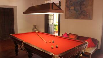 Una mesa de billar con bolas, un sofá con cojines y un cuadro en la pared.