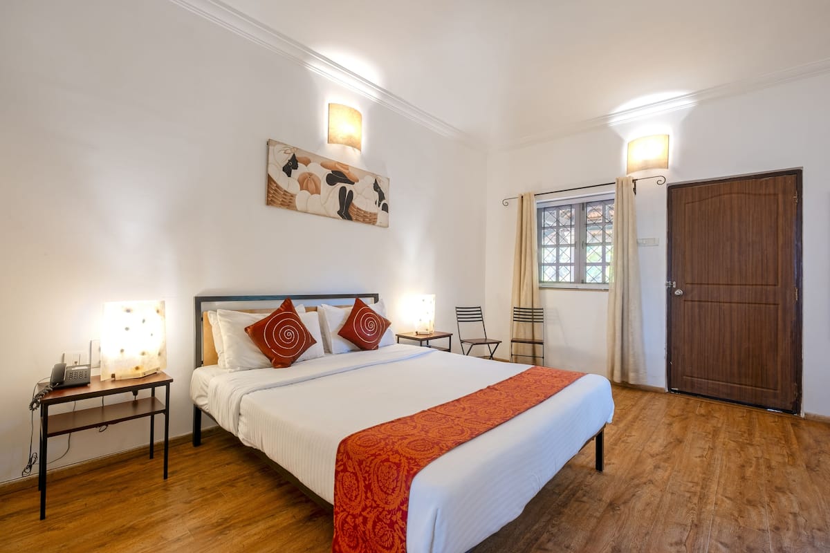 A hotel room with a large bed, two bedside tables with lamps, a wooden floor, a door, and a window with curtains.