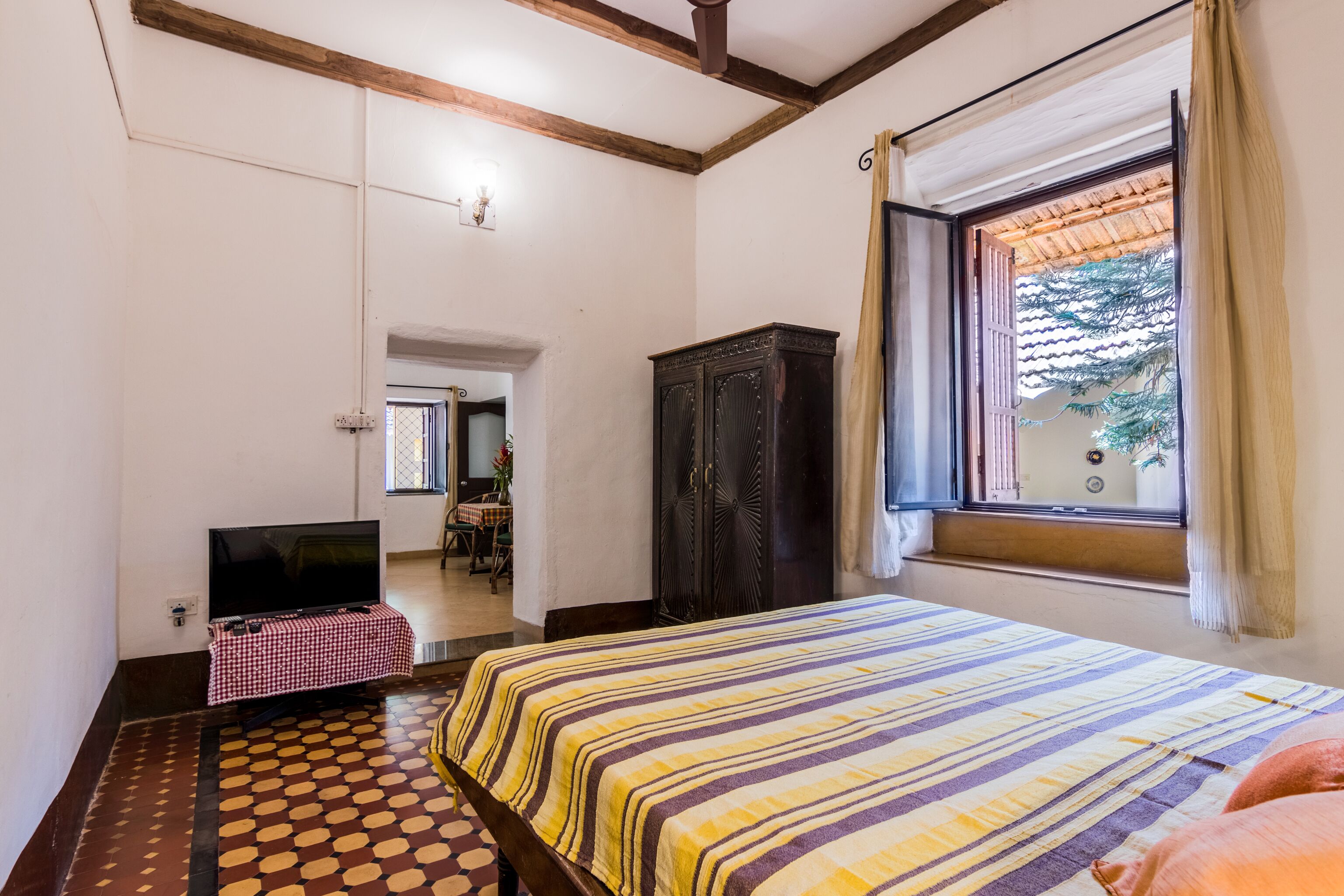 Un dormitorio con cama, televisión, armario y ventana con cortinas.