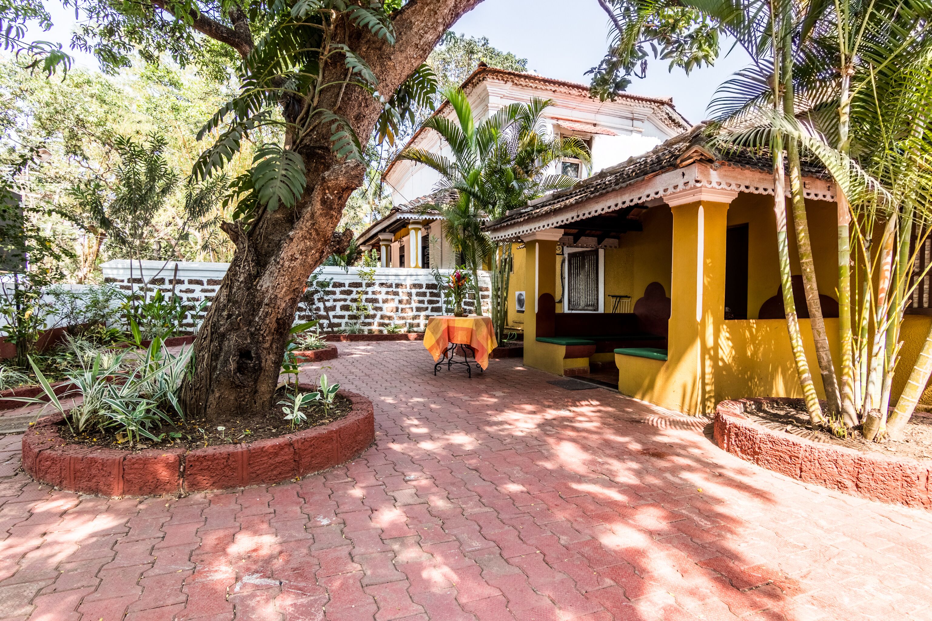 A courtyard with a paved walkway, a covered seating area, and a building with a tiled roof.
