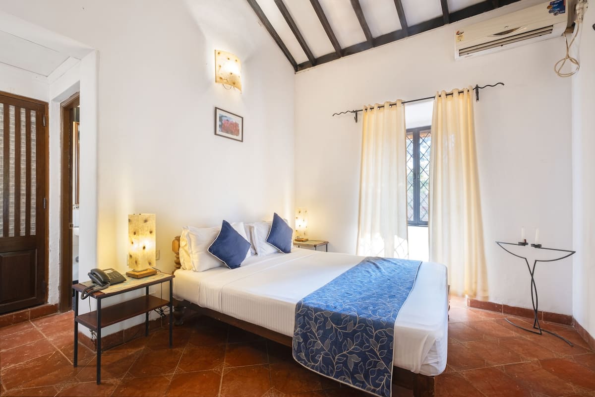 A bedroom with a bed, bedside tables, a telephone, a wall-mounted light, a window with curtains, and a ceiling fan.