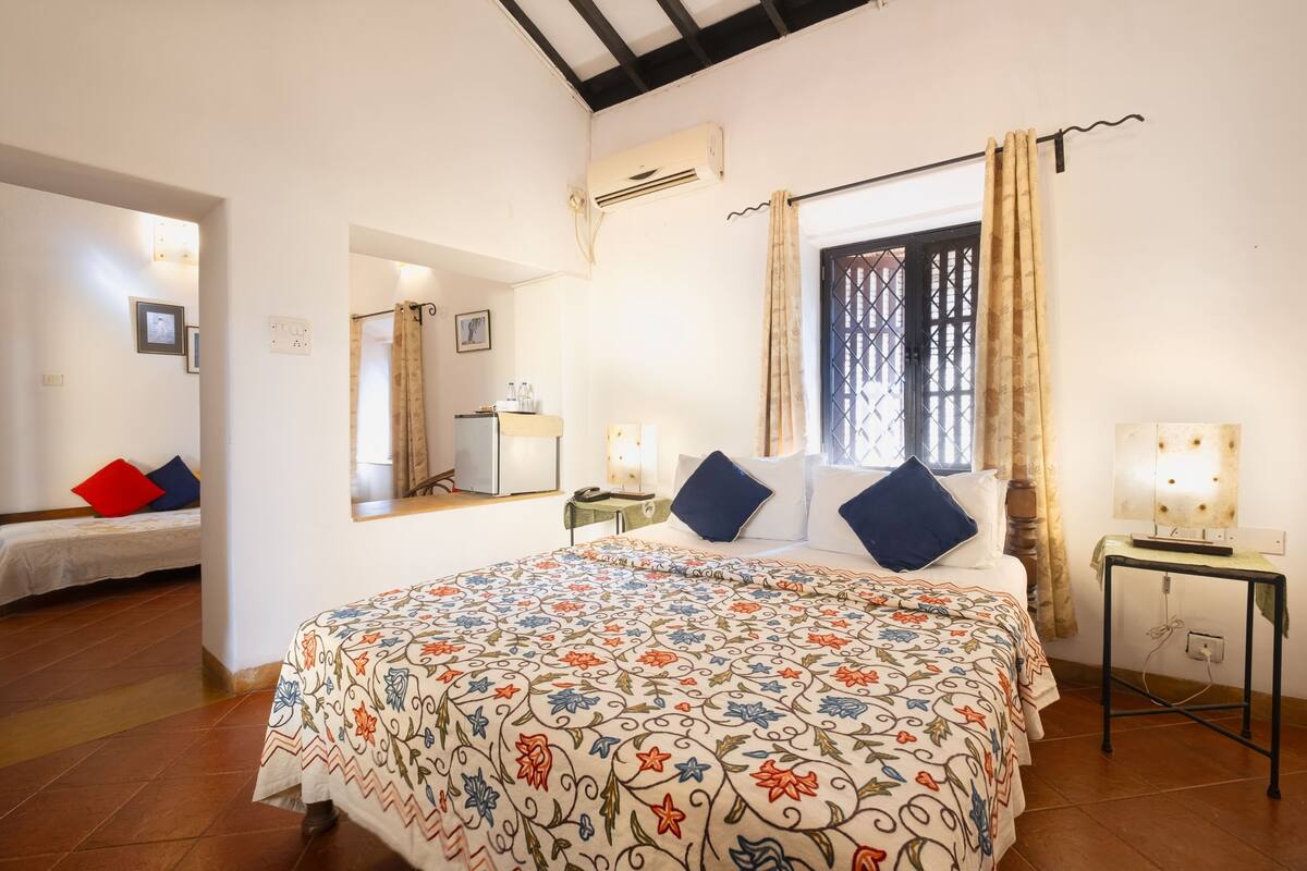 A bedroom with a large bed, a bedside table, a nightstand, a mirror, and a window with curtains.