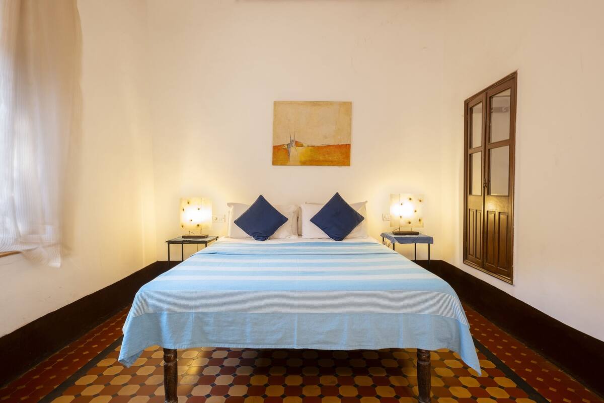 A hotel room with a bed, two bedside tables, two lamps, a painting on the wall, and a door.