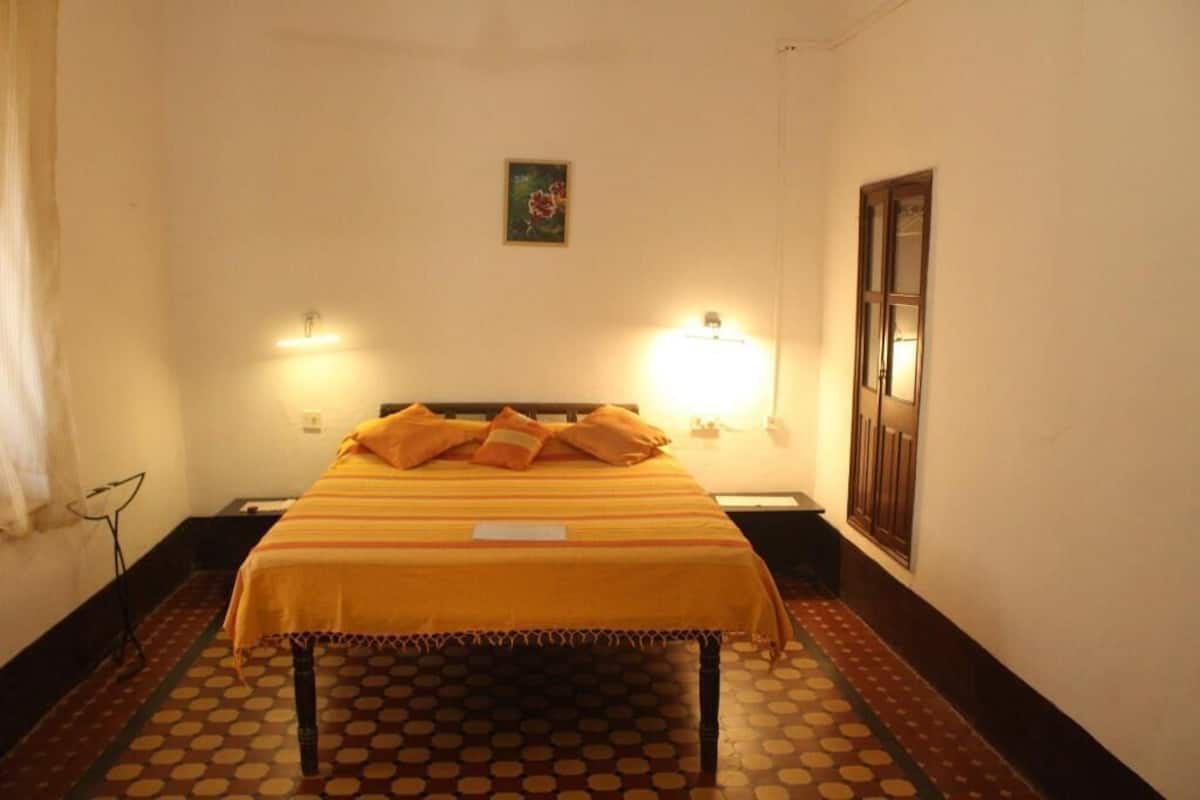 A single bed with a striped bedspread, two wall-mounted lamps, a small framed picture on the wall, and a patterned floor.