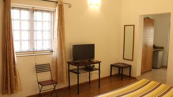 Una habitación con cama, televisión sobre un mueble bajo, una silla, una mesita y un espejo en la pared.