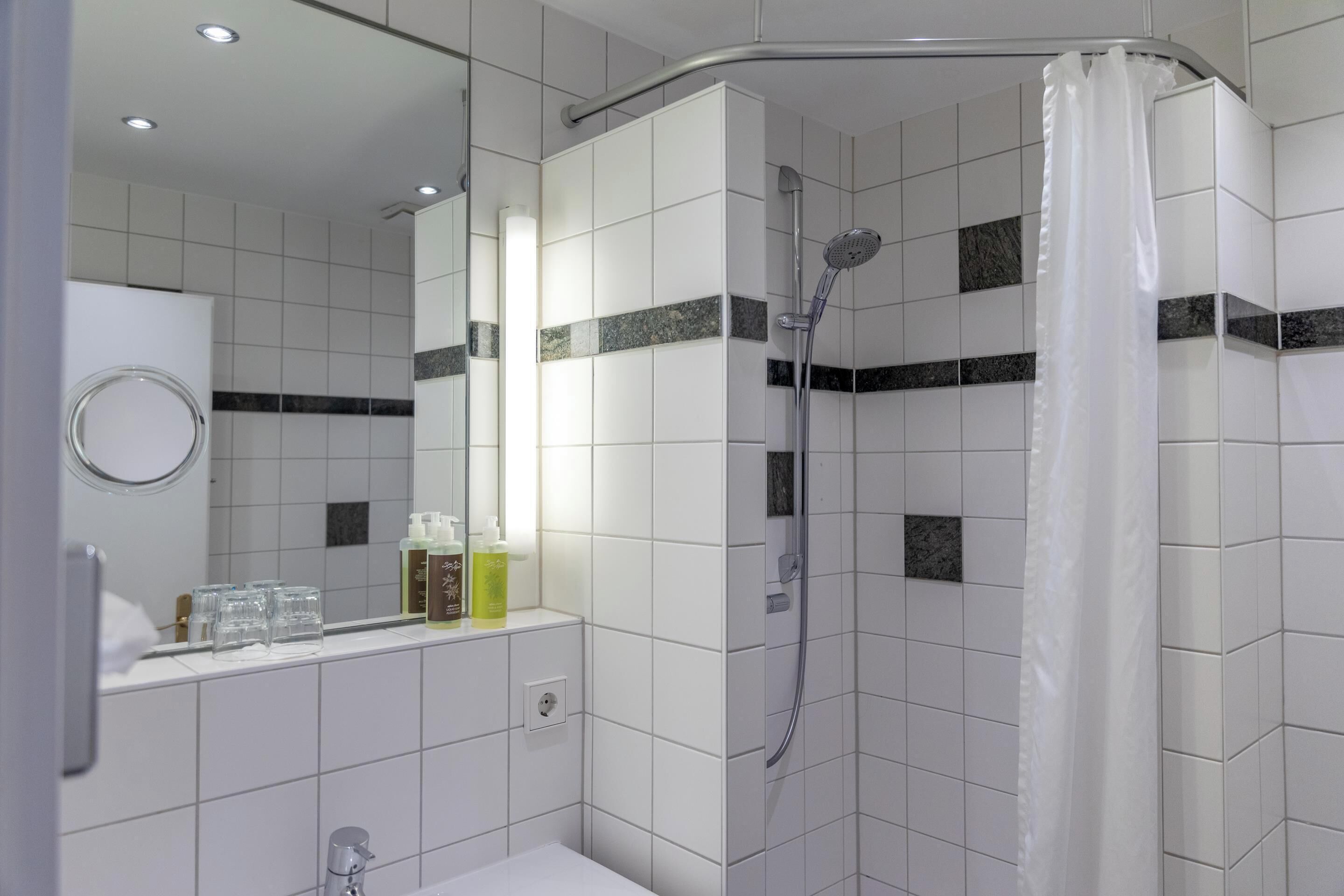 Un baño moderno con azulejos blancos, ducha, lavabo y espejo.