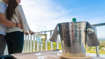 A table with a metallic container and two glasses of white wine, set against a scenic outdoor backdrop.