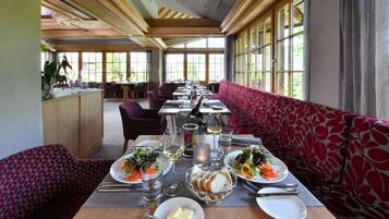 Un restaurant avec une longue table à manger dressée pour le repas, entourée de sièges aux motifs rouges.