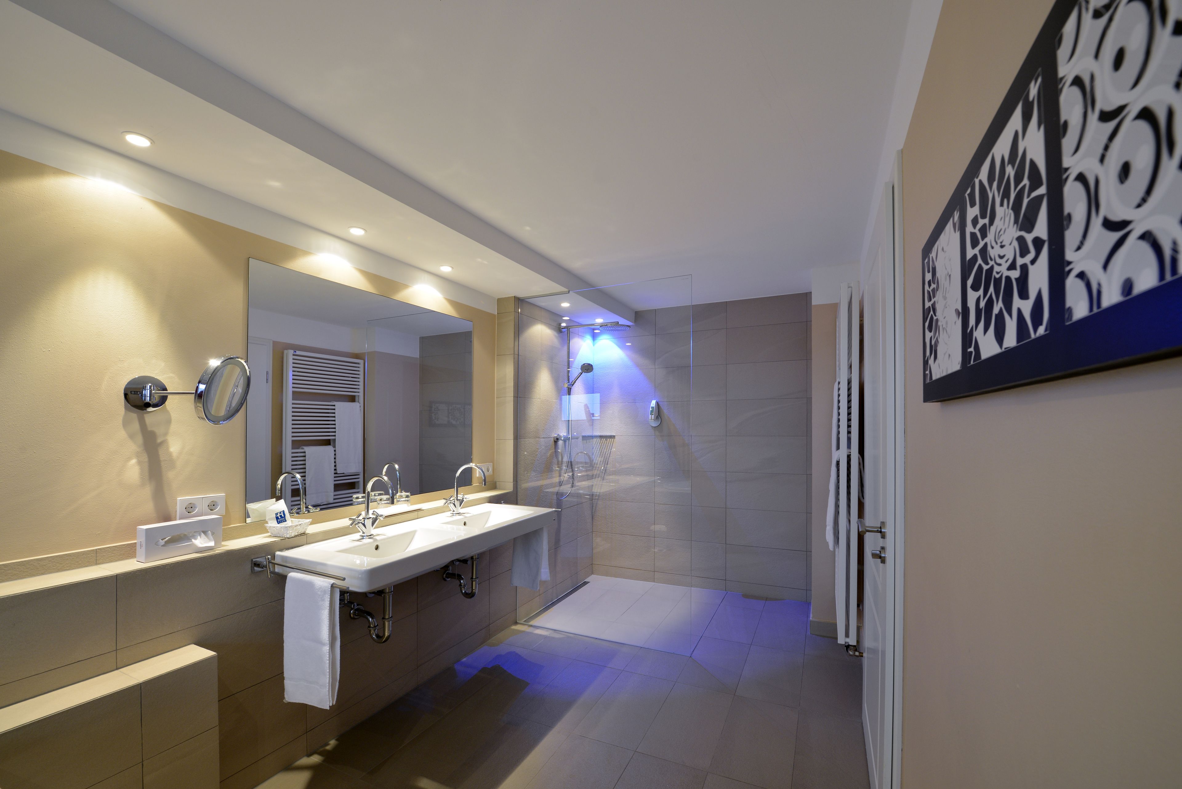 A modern bathroom with two sinks, a large mirror, and a shower area.