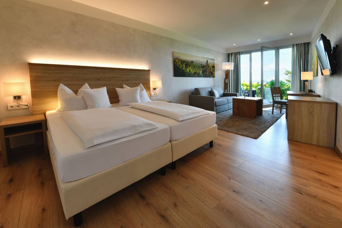 A modern hotel room with a large bed, a sofa, a desk, and a TV.