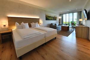 Quarto de hotel moderno com uma cama grande, um sofá, uma escrivaninha e uma televisão.