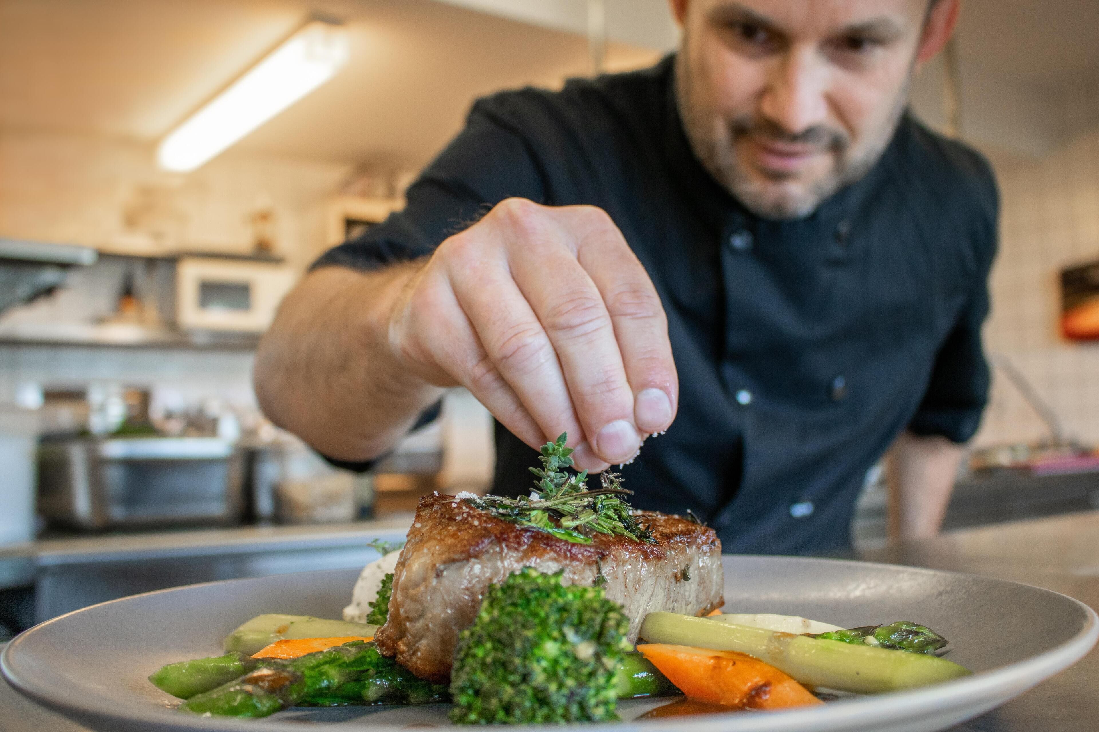 A chef seasoning a dish with herbs.
