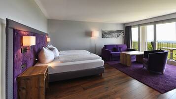 A modern bedroom with a large bed, a small sofa, a table, and a balcony with a view.