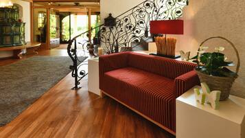 A modern living room with a red sofa, a wooden floor, a staircase with ornate railings, and a view of a garden through an open door.
