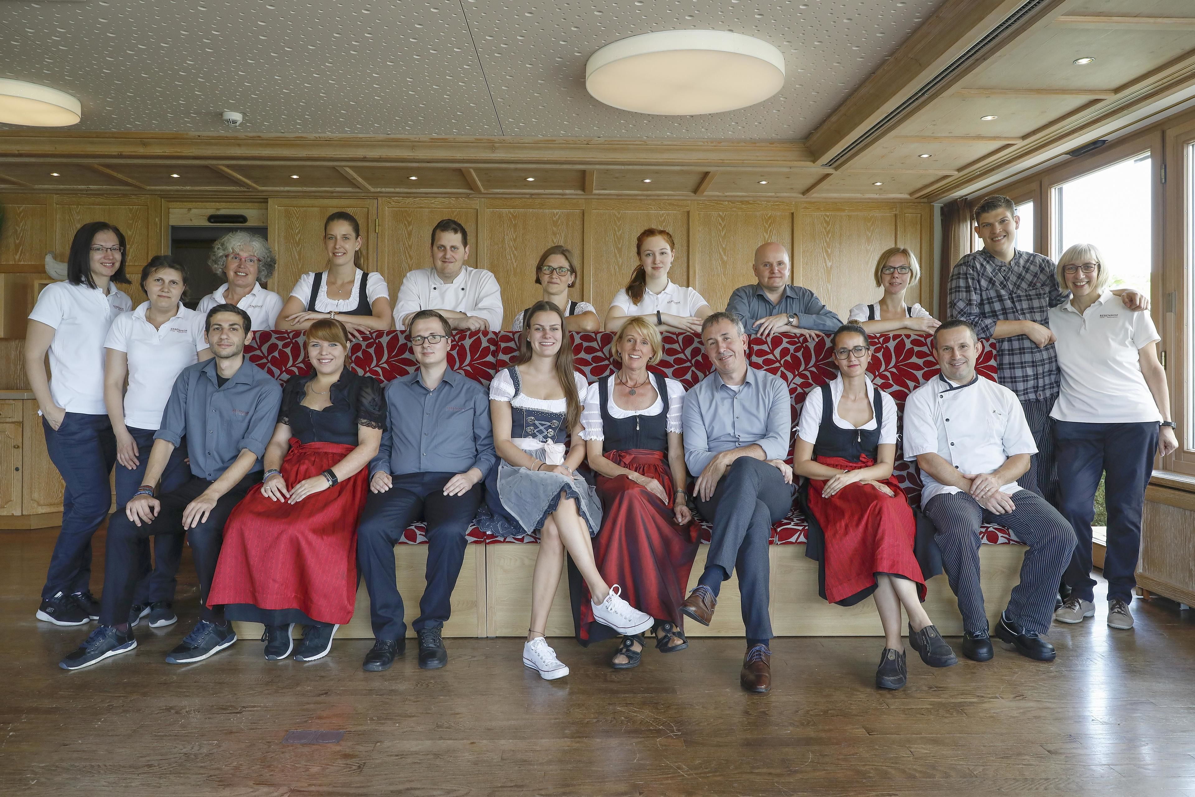 Un grupo de personas sentadas y de pie en una habitación con paneles de madera y un ventanal grande.