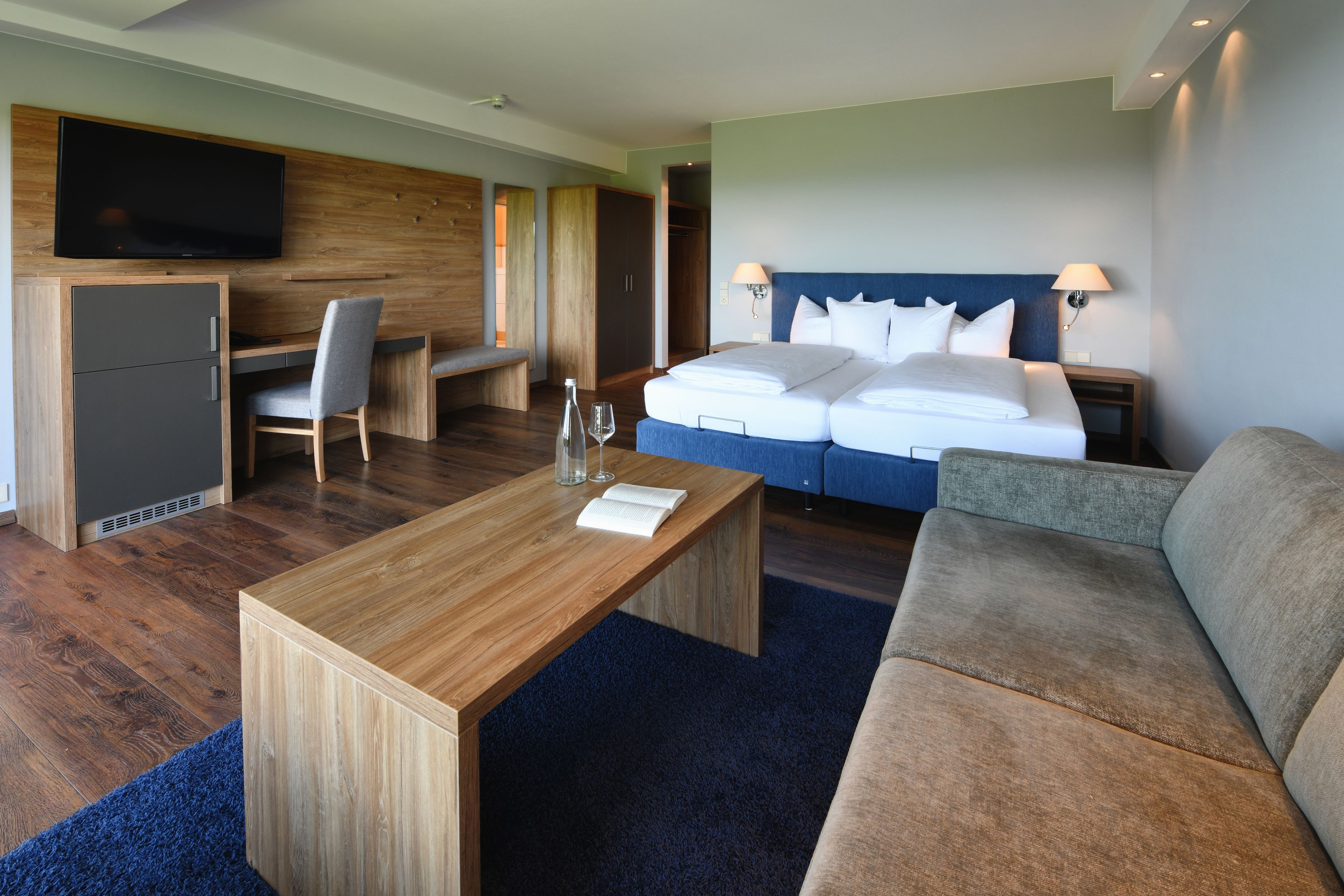 A hotel room with a bed, a desk, a TV, and a seating area.