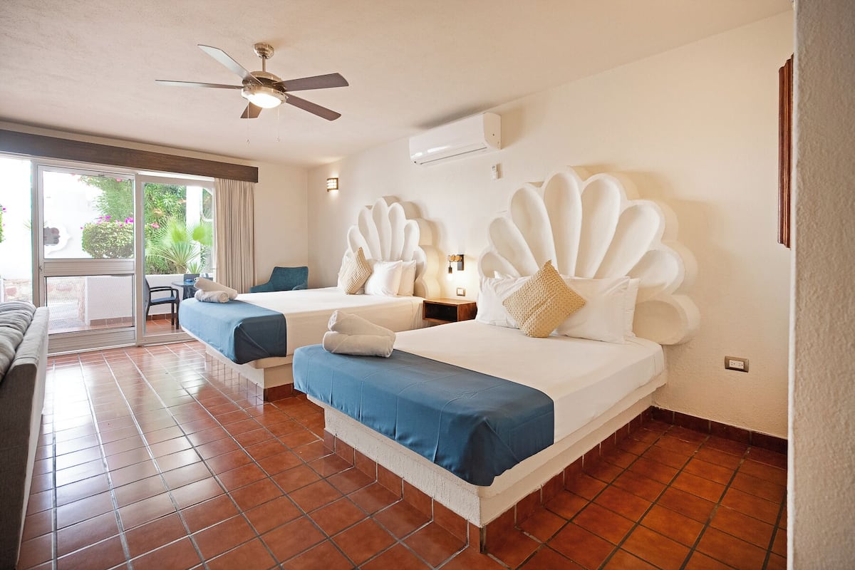 Habitación de hotel con dos camas, ventilador de techo, aire acondicionado y vistas al exterior.