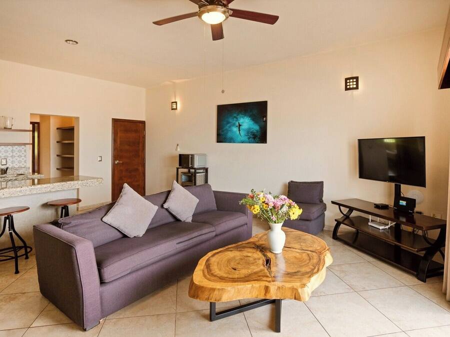 A modern living room with a sofa, coffee table, TV, and kitchen area.