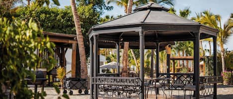 A gazebo with a roof, surrounded by palm trees and outdoor seating.