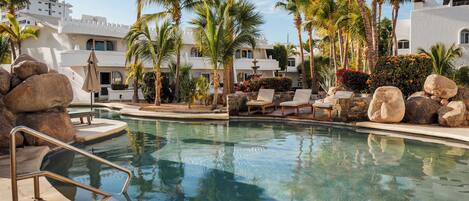 Une piscine bordée de palmiers, avec des chaises longues et une fontaine en pierre.