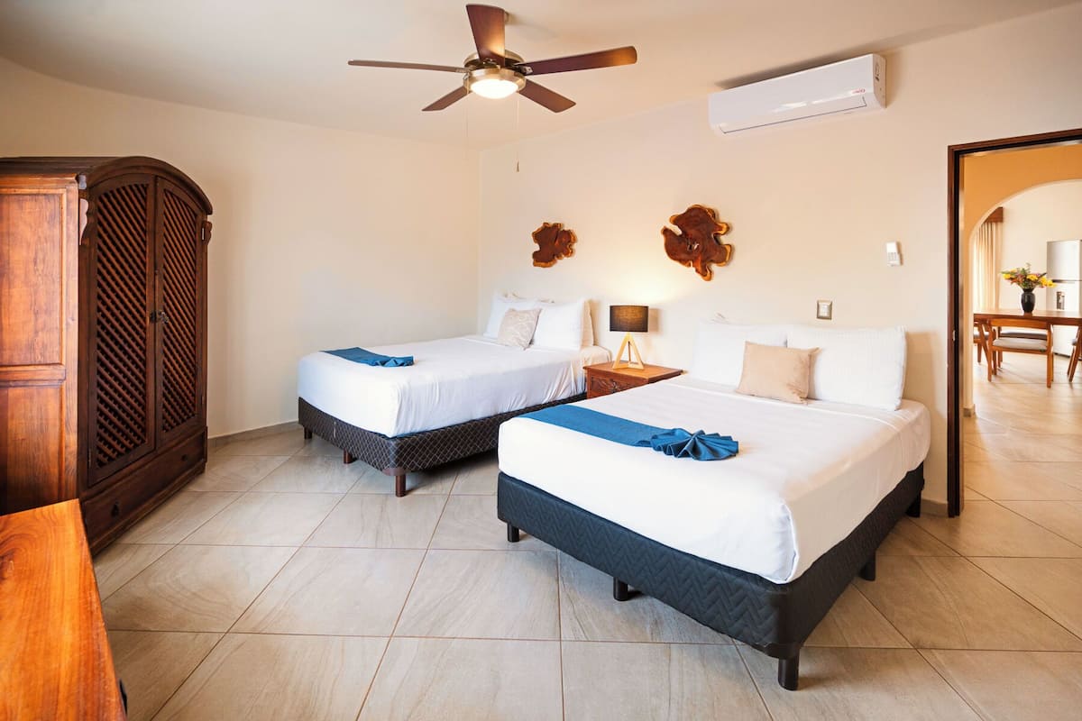 Habitación de hotel con dos camas, ventilador de techo, aire acondicionado y un armario de madera.