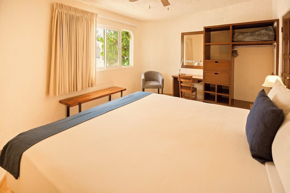 Un dormitorio con cama, escritorio, silla, banco y armario.