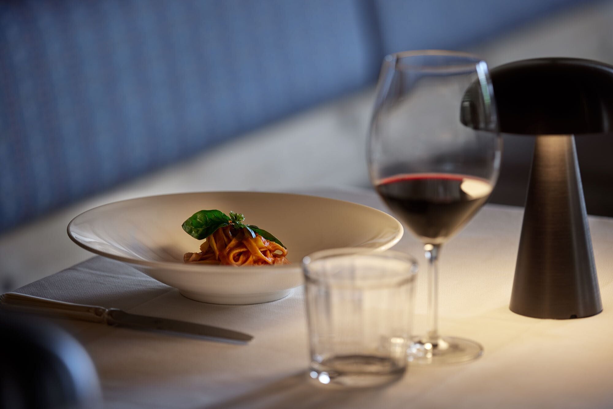 A dining table with a bowl of pasta, a wine glass, and a pepper grinder.