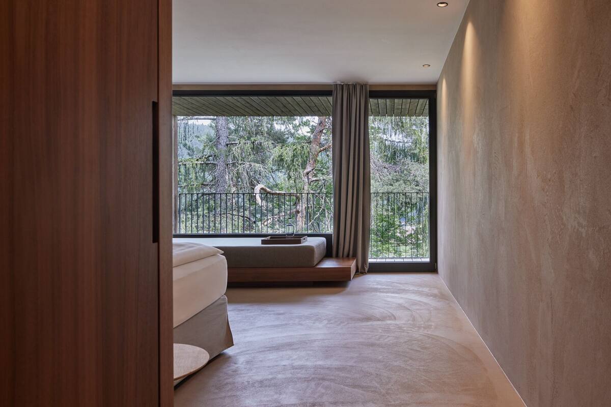 Une chambre d’hôtel moderne dotée d’une grande fenêtre, d’un canapé et offrant une vue sur les arbres, ainsi qu’un balcon.