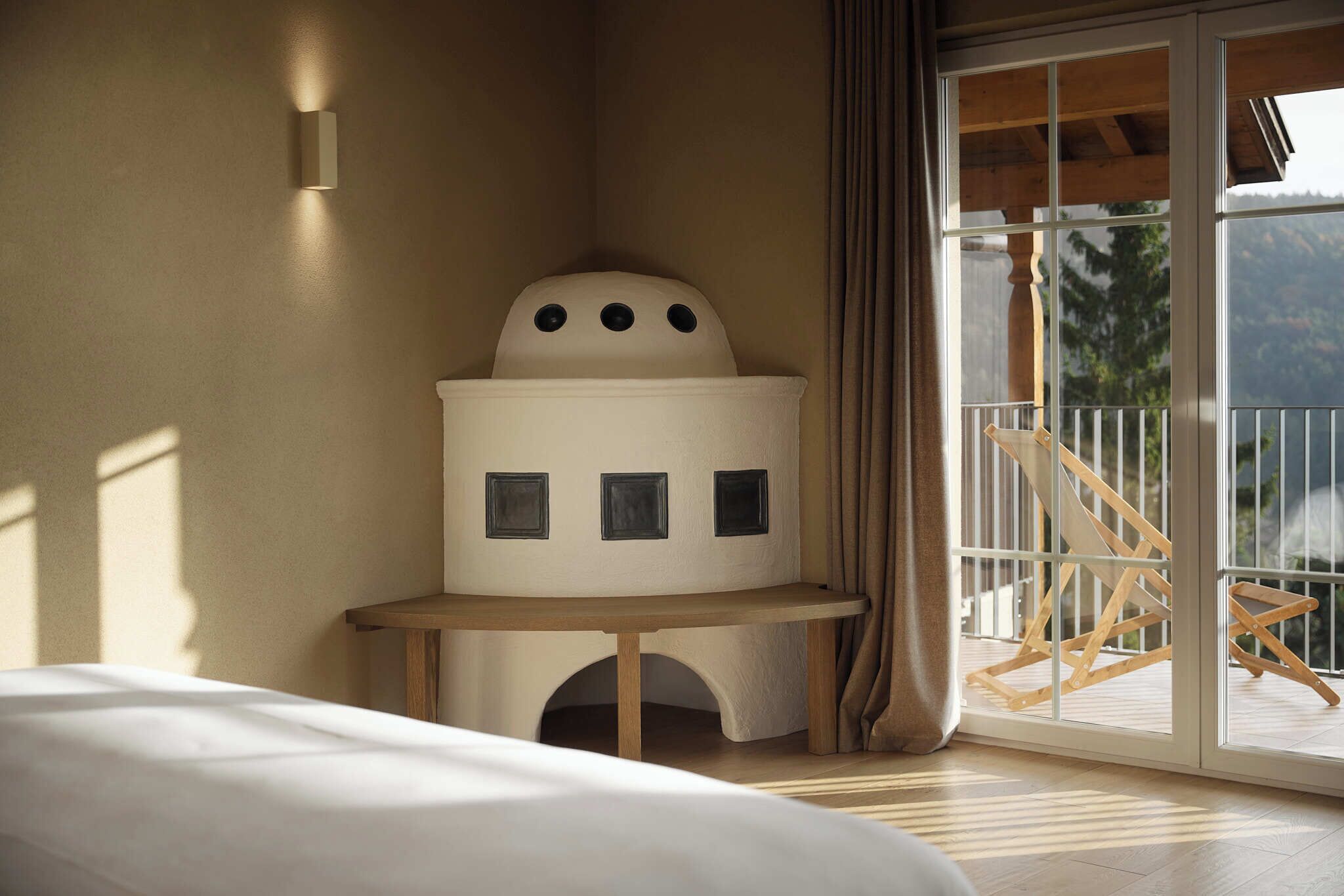 Ein Schlafzimmer mit Bett, einem kleinen Tisch, einer Wandlampe, einem großen Fenster mit Blick ins Freie und einem Balkon mit einem Holzstuhl.